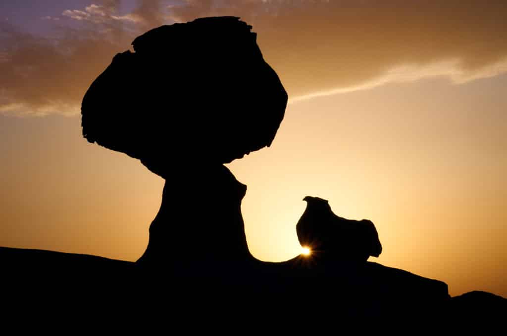 The giant boulder appears to be supported by something strong enough to hold it up. Silhouette against open sun-setting sky. The purpose of this image is to represent supporters, a sustainable scholarly communication future that promises greater openness and innovation under the academic community's direction.